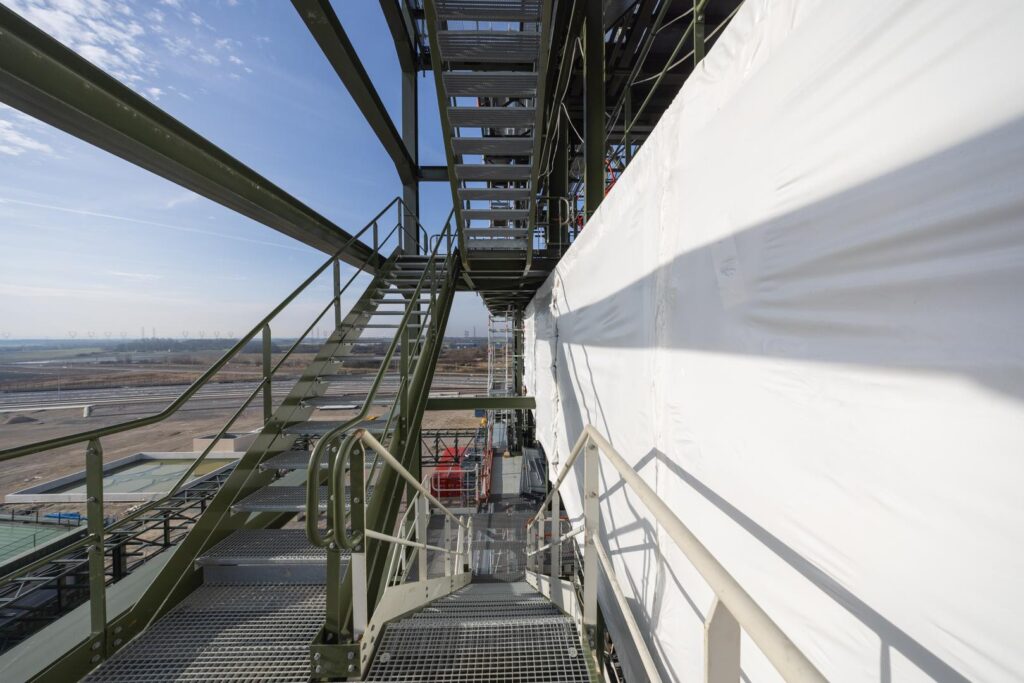 Tour d'accès et escalier d'échafaudage sécurisé installés sur un chantier industriel de grande hauteur avec bâche de protection.